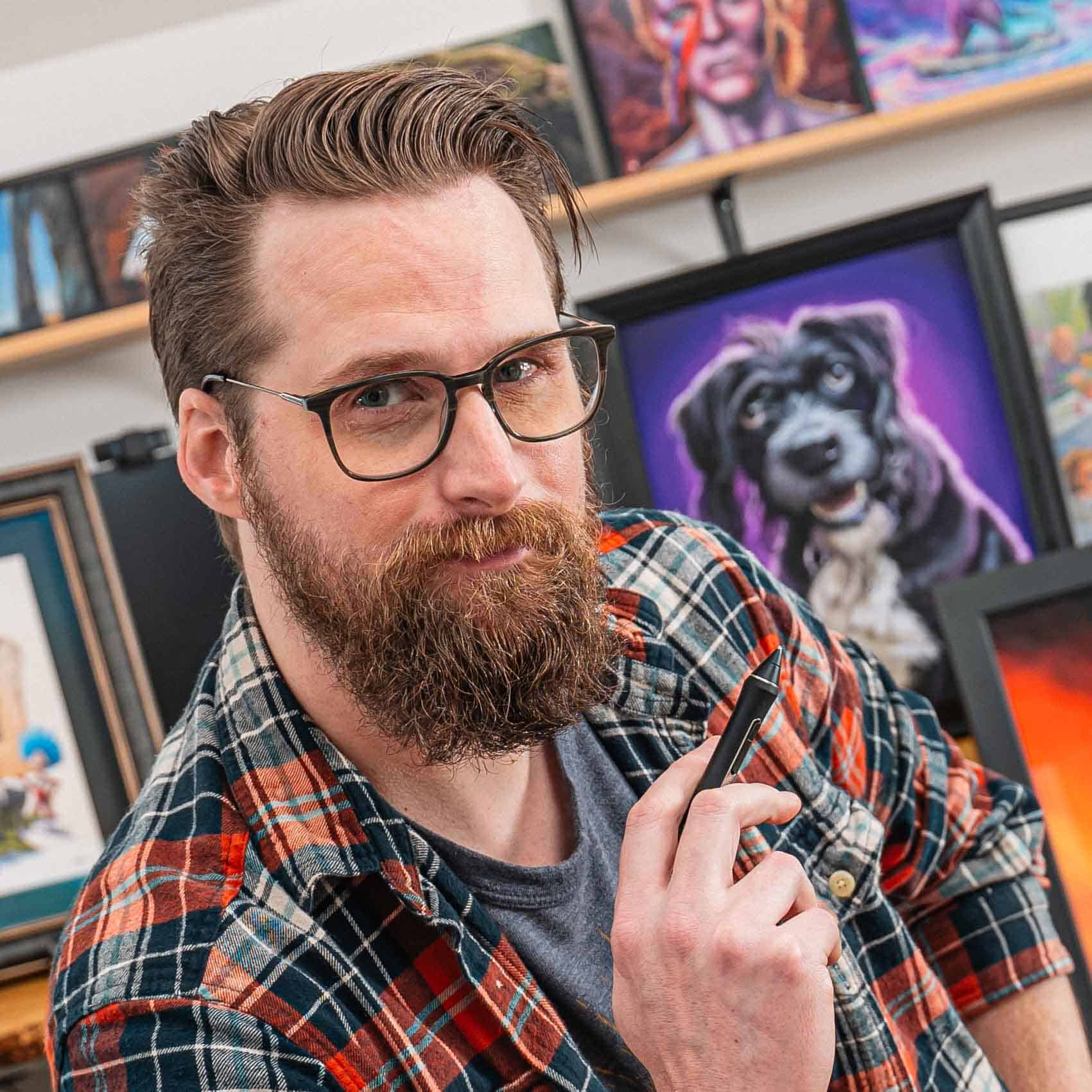 Headshot of artist Ian Moss wearing glasses and a plaid shirt holding a paint brush